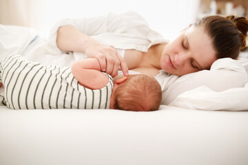 Cute caucasian mom and newborn baby, mom breastfeeds her baby lying on a white background on the bed in the bedroom, close-up, soft focus