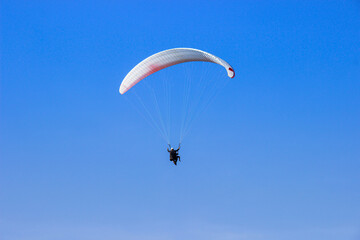 Tourist flying on a paraglider flying in the blue sky on a bight day. The sportsman paragliding.