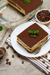 Traditional Italian Tiramisu dessert in glass baking dish and portion on grey concrete background