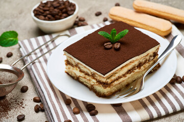 Portion of Traditional Italian Tiramisu dessert and coffee beans on grey concrete background