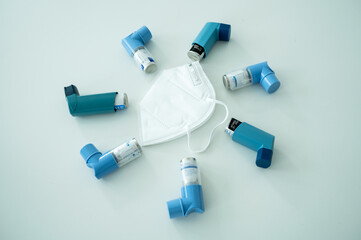 Various asthma spray inhalers and a Covid-19 respirator mask on a white surface	
