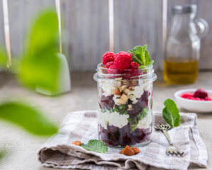 A healthy salad with beets, cream cheese or cottage cheese, nuts and raspberries in a glass jar on a light concrete background. Salad recipes.