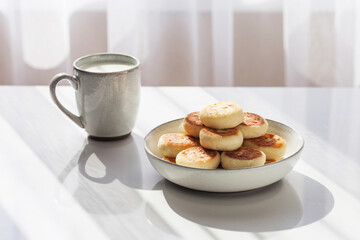 Plate of pancakes and a cup of milk on the white table. Healthy breakfast or lunch. Sunlight and shadow. Copy space. Top view