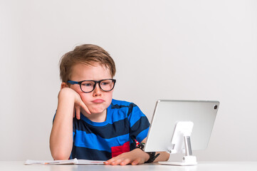 Online school education. Pupil with tablet computer. Kid in glasses writing book sitting at the...