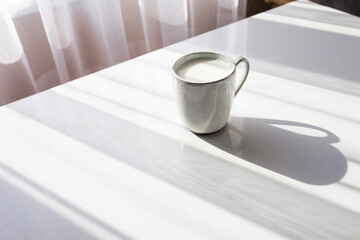 Сup of milk on the white table. Healthy breakfast or lunch. Sunlight and shadow. Copy space