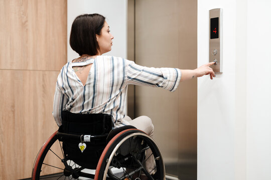 White young woman pushing button while sitting in wheelchair by elevator