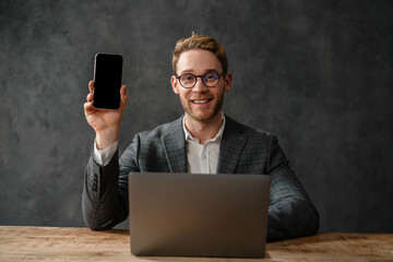 The smiling man showing the phone screen to the camera while sitting in the studio