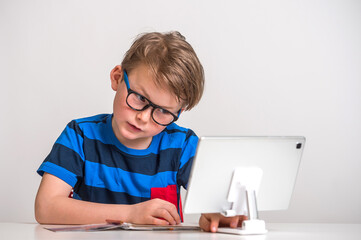 Young little caucasian kid in blue striped shirt has online school lesson with teacher on computer....