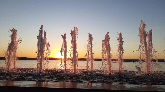 Fountain at sunset, slow motion, water jets rise up against the sunset, the sun goes down