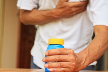 Old Man clutching his chest from acute pain and pick up his medication.Sublingual pill for relieve symptom of heart attack.Emergency condition.Healthcare and medical concept.