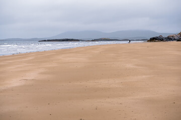 Fototapeta na wymiar Empty sandy beach at low tide and blue water of Atlantic ocean. West coast of Ireland. Cloudy low sky. Irish nature landscape