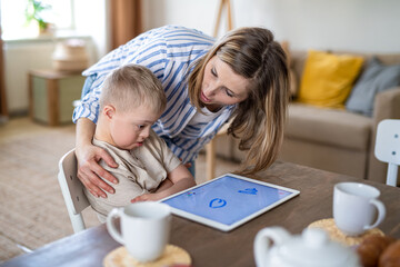 Obraz na płótnie Canvas Single mother and upset down syndrome son with tablet at home, distance learning.