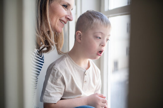 Single mother with down syndrome child at home, looking out of window.