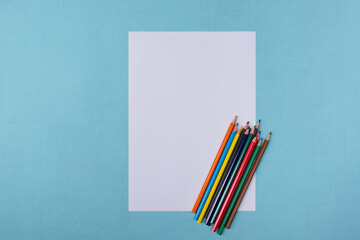 A blank white sheet and colored pencils for drawing on a plain textured background with space for copying and lettering.