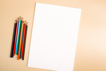A blank white sheet and colored pencils for drawing on a plain textured background with space for...