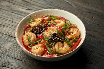 Delicious Asian street food - funchose noodles with shrimp, cilantro, vegetables and omelet in a white bowl on a wooden background. TCellophane noodles wok