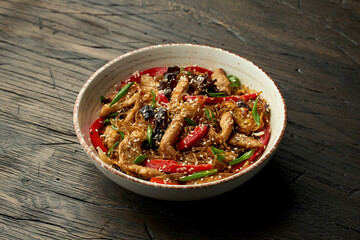 Delicious Asian street food - funchose noodles with chicken, cilantro, vegetables and omelet in a white bowl on a wooden background. Cellophane noodles wok