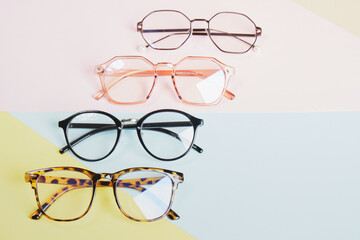 multiple eyeglasses on a multicolored background of pastel colors, geometric background, pink yellow and light blue colors, trendy eyeglass frames
