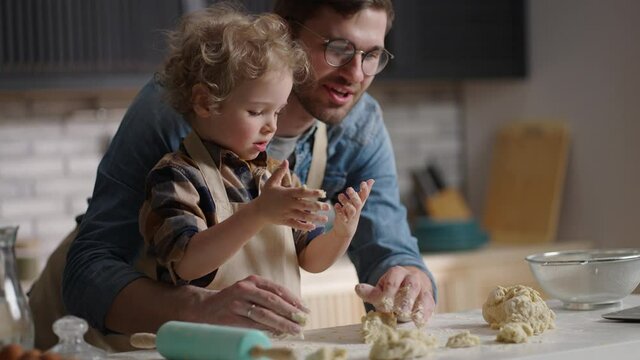 cheerful dad and his little son with funny light curls are cooking at home kitchen together, medium portrait of happy family