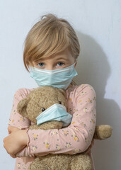 This girl is in a medical mask and holding a teddy bear. The teddy bear is in a mask.