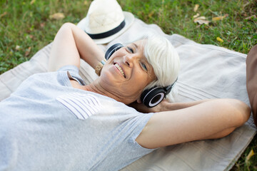 Obraz na płótnie Canvas mature woman wearing headphones laid on grass