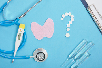 silhouette of the thyroid gland cut out of pink felt, a question mark from pills, a thermometer, ampoules and a stethoscope , diagnostics and treatment of thyroid diseases concept