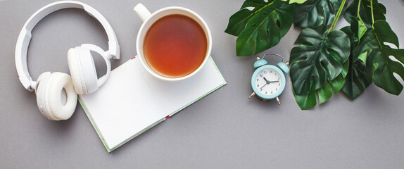 Workplace with notepad, headphones,cup of tea or coffee, alarm clock and green plant monstera. Freelancer working space