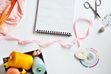 Sewing materials - a box with threads of bright colors, a pink ribbon, as well as a notebook for text on a white background. Frame, space for text