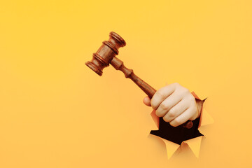 Hand holding a judge's gavel through torn yellow paper wall. Law and courts, triumph of justice