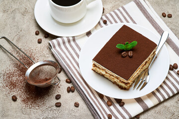Portion of Traditional Italian Tiramisu dessert and cup of coffee on grey concrete background