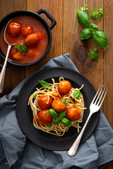 Spaghetti with eatballs tomato sauce , basil leaves in black mate plate on wooden background, delicious mediteranean food