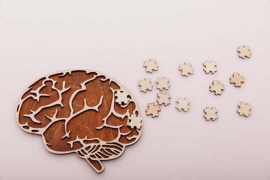 Alzheimer's disease and mental health concept. Brain and wooden puzzle on a pink background