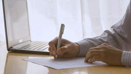 Hand of a man writing a document. Notebook computer on the desk.