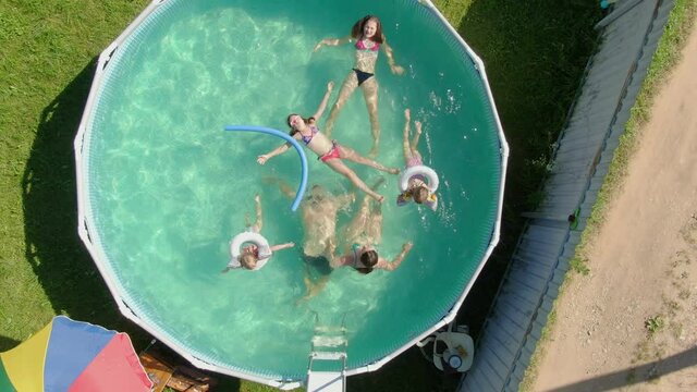 A group of children is swimming and having fun in the blue round swimming pool in the backyard. Aerial shooting of backyard swimming pool