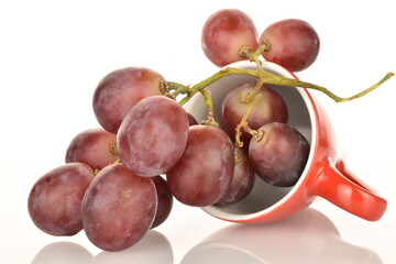 A bunch of fresh organic, juicy, ripe, sweet grapes with a ceramic red cup, close-up, on a white background.