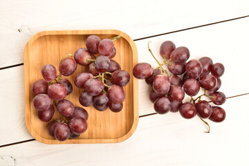Two bunches of fresh organic, juicy, ripe, sweet grapes with a bamboo tray, close-up, on a painted table made of wood.
