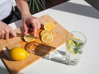 Woman cutting lemon on wooden board. Detox water with mint and lemon. Refreshing summer drink....