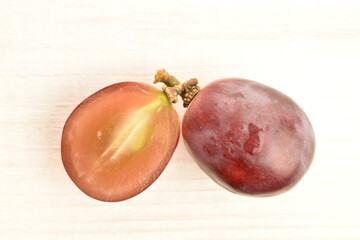 One whole and one half, fresh organic, juicy, ripe, sweet grapes, close-up, on a table of painted natural wood.