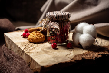 A jar and cookies with berries lie on a wooden board on a brown background