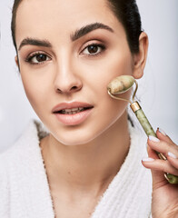 Portrait of a brunette woman using jade or stone roller for a facial lifting procedure. Close-up