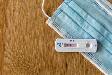 COVID-19 Rapid Antigen Test and a surgical mask on a wooden table. Concept of a broad testing strategy and prevention measures to cope with the pandemic.