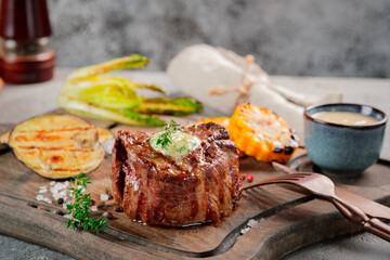 Large grilled Filet Mignon steak with butter and thyme served on a wooden board. Grilled meat dish with vegetables