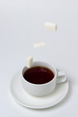 Sugar cubes fall into a cup of tea on a white background. A cup of tea with refined sugar. Tea time