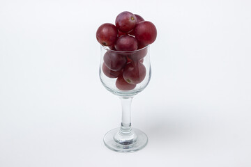 Pink grapes in a wine glass on a light background. Large pink grapes on white background
