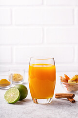 Healthy drink from turmeric and ginger roots and lime in a glass on white concrete background.