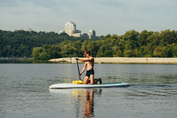 Athletic young man kneels on a sup board and swims on the river against the backdrop of a beautiful...
