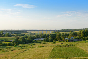 Obraz premium Summer evening landscape with a railway bridge, a green ravine with a village