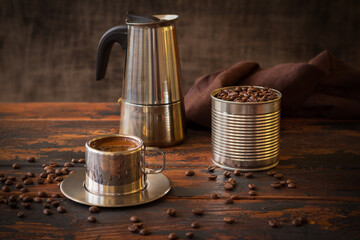 Steel cup of coffee, blended coffee beans in a tin can and geyzer coffee maker, brown napkin on a...