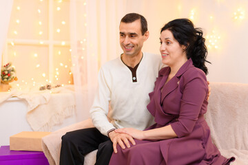 portrait of adult romantic couple sitting on a couch in home interior decorated with lights
