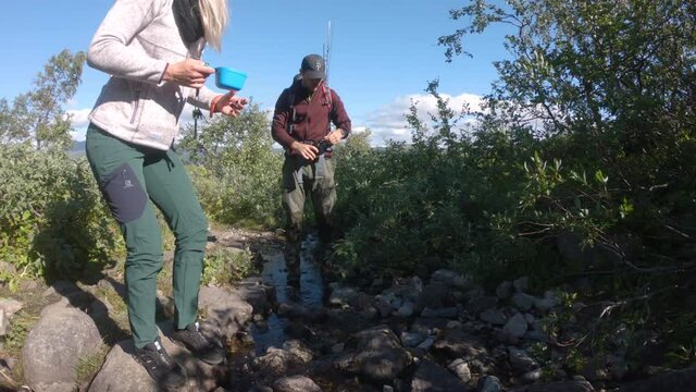 Man and woman hiker taking a break and drinks water from a small stream in the beautiful nature of Saltoluokta, Northern Sweden.